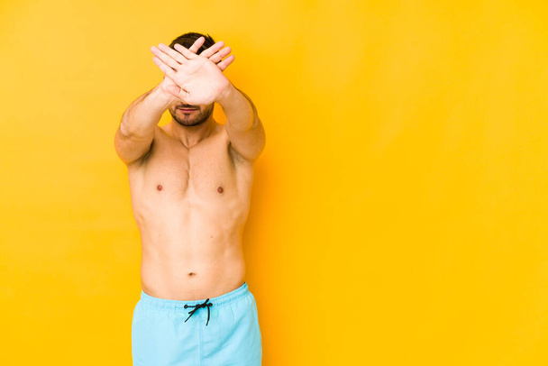 Молодий білий чоловік з купальником ізольований на жовтому тлі Молодий білий чоловік з триманням двох схрещених рук, заперечення концепції
. - Фото, зображення