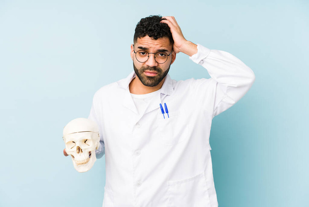 Young doctor latin man holding a skull isolated being shocked, she has remembered important meeting. - Photo, Image