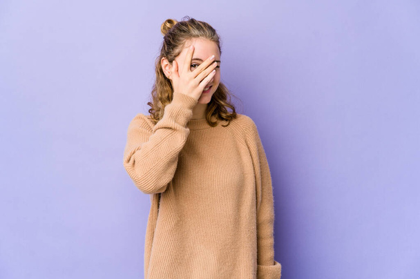 Young caucasian woman on purple background blink at the camera through fingers, embarrassed covering face. - Fotoğraf, Görsel