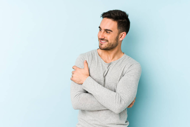 Young caucasian man isolated on blue background smiling confident with crossed arms. - Foto, imagen