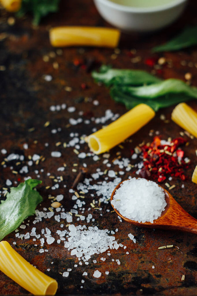 Sea salt in wooden spoon surrounded by pasta and other ingredients - Foto, immagini