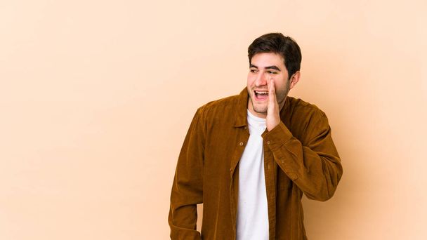 Young man isolated on beige background shouting excited to front. - Фото, изображение
