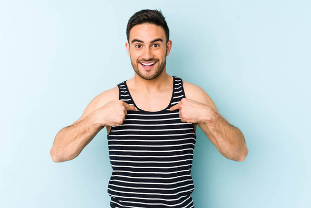 Young caucasian man isolated on blue background surprised pointing with finger, smiling broadly. - Foto, imagen