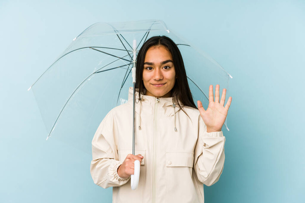 Молода азіатка тримає парасольку усміхненою веселою, показуючи номер п'ять пальцями
. - Фото, зображення