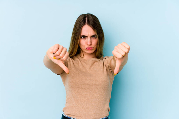 Young caucasian woman isolated on blue background showing thumb down and expressing dislike. - Foto, Imagem
