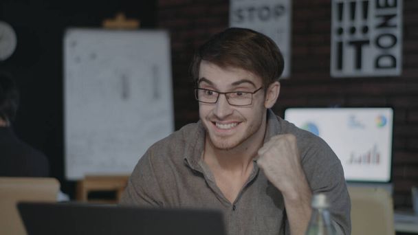 Uomo d'affari allegro guardando lo schermo del computer portatile e facendo sì gesto in ufficio scuro - Foto, immagini