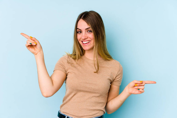 Giovane donna caucasica isolata su sfondo blu che punta a diversi spazi di copia, scegliendo uno di loro, mostrando con il dito. - Foto, immagini