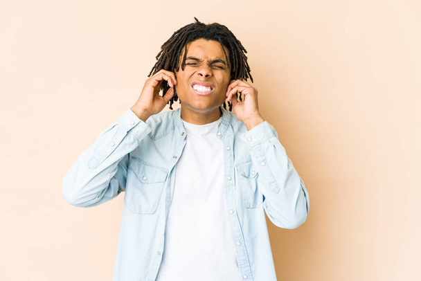 Νεαρός Αφροαμερικάνος ραστάς που καλύπτει τα αυτιά του με δάχτυλα, αγχωμένος και απελπισμένος από ένα δυνατό περιβάλλον. - Φωτογραφία, εικόνα