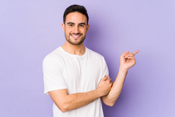 Young caucasian man isolated on purple background smiling cheerfully pointing with forefinger away. - Photo, Image