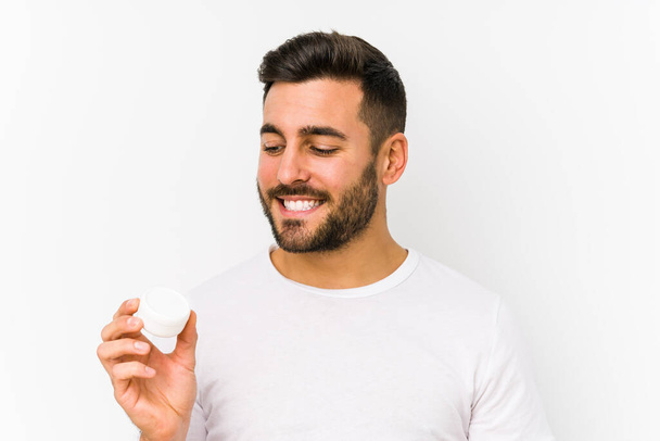 Young caucasian man holding a moisturizer isolated smiling confident with crossed arms. - Photo, Image