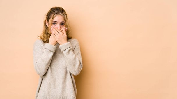 Young caucasian woman isolated on beige background covering mouth with hands looking worried. - Foto, Imagem