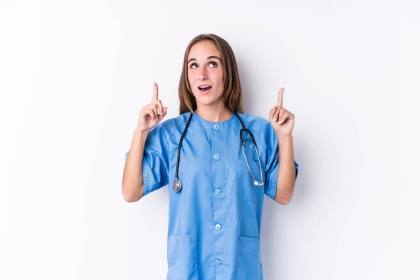 Молодая медсестра женщина изолированы указывая вверх ногами с открытым ртом. - Фото, изображение