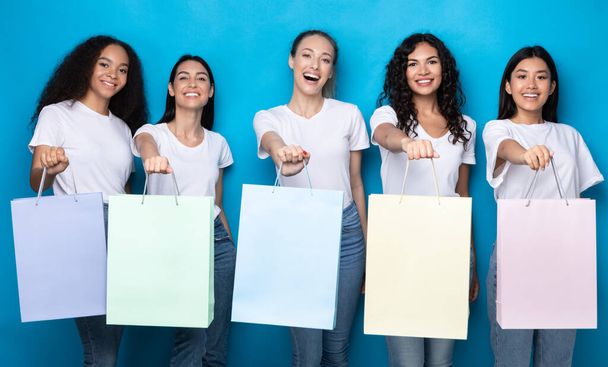 ブラックショッピングバッグを示す5人の女性が青の背景に立つ - 写真・画像
