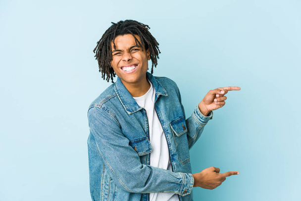 Young black man wearing a jeans jacket pointing with forefingers to a copy space, expressing excitement and desire. - Photo, Image