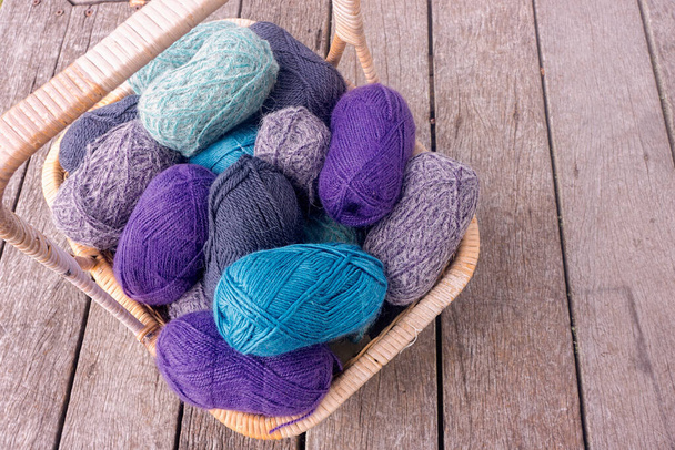 Basket of knitting wool in shades of purple,grey and blue ready to make a garment sitting on an old wooden deck. - 写真・画像