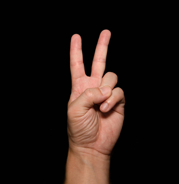 A mão do homem que segura dois dedos é um sinal V, que significa vitória. Ou ainda significa paz e desprezo pelos desafios no fundo preto - Foto, Imagem