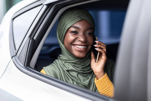 Μαύρη μουσουλμάνα που ταξιδεύει στο πίσω κάθισμα του αυτοκινήτου και μιλάει στο κινητό - Φωτογραφία, εικόνα
