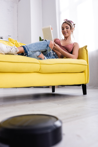 Selective focus of woman lying on couch and robotic vacuum cleaner - Φωτογραφία, εικόνα