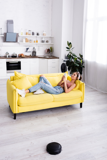 Woman lying on couch and using smartphone - Foto, afbeelding