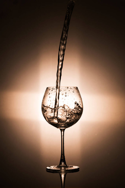 Verter agua en la copa de vino con luz trasera sobre fondo negro  - Foto, Imagen