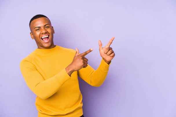 Young latin man isolated on purple background pointing with forefingers to a copy space, expressing excitement and desire. - Fotoğraf, Görsel