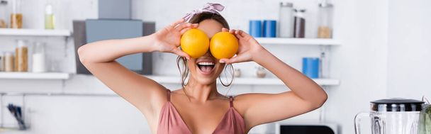 Website header of woman holding oranges near eyes at home  - Фото, изображение