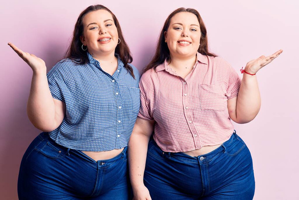 Young plus size twins wearing casual clothes smiling cheerful presenting and pointing with palm of hand looking at the camera.  - Photo, Image