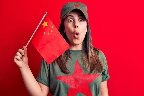 Gyönyörű hazafias nő visel póló piros csillag kommunista szimbólum kezében porcelán zászló rémült és csodálkozott nyitott szájjal meglepetés, hitetlen arc - Fotó, kép