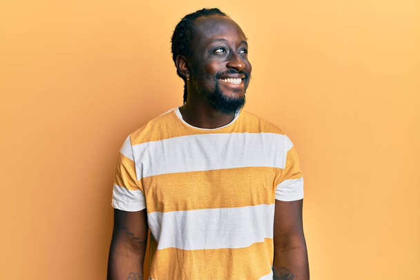 ハンサムな若い黒人男性の顔に笑顔で横に見てカジュアルな黄色のTシャツを着て、自然な表情。自信を持って.  - 写真・画像