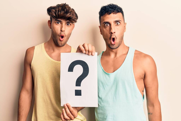 Mladý gay pár držící otazník vyděšený a ohromený s otevřenými ústy pro překvapení, nevěřící tvář  - Fotografie, Obrázek