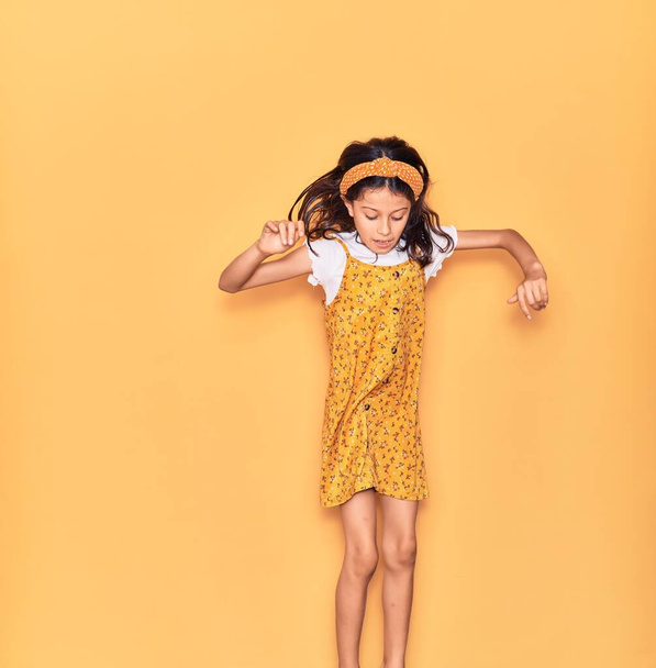 Adorable hispanic child girl wearing casual dress and diadem smiling happy. Jumping with smile on face over isolated yellow background - Fotografie, Obrázek