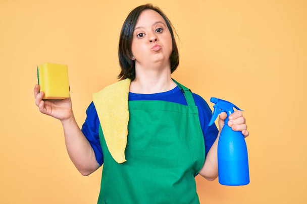 Brunette woman with down syndrome wearing apron holding scourer looking at the camera blowing a kiss being lovely and sexy. love expression.  - Photo, Image
