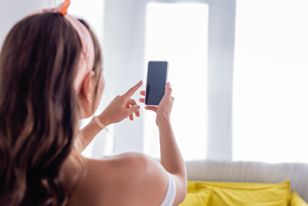 自宅で空白の画面を持つスマートフォンを使用して若い女性の選択的な焦点  - 写真・画像