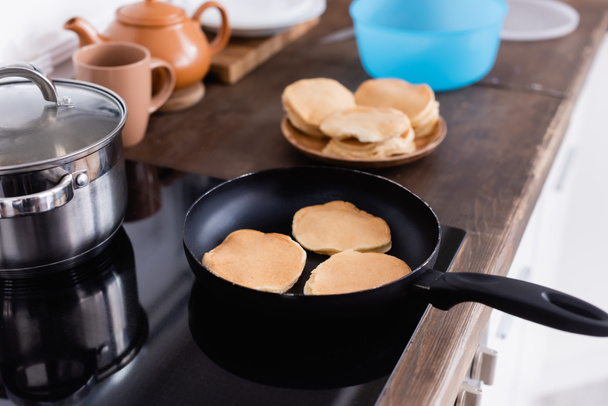 Selective focus of pancakes on frying pan on stove in kitchen  - Valokuva, kuva
