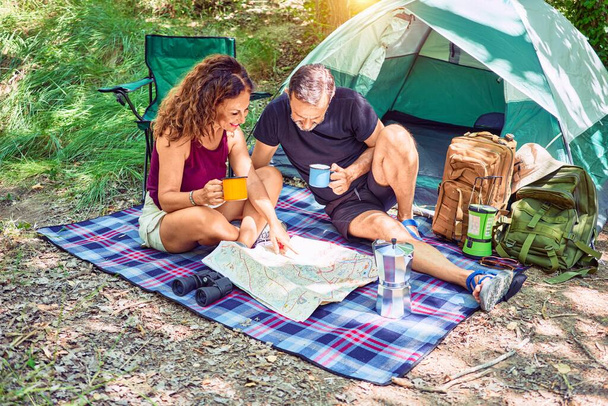 Middle age couple  of hiker smiling happy drinking coffee. Looking at the map camping at the forest - Foto, afbeelding