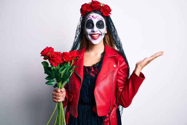 Vrouw draagt dag van het dode kostuum met rozen die de overwinning vieren met een vrolijke glimlach en een winnaarsuitdrukking met opgeheven handen  - Foto, afbeelding