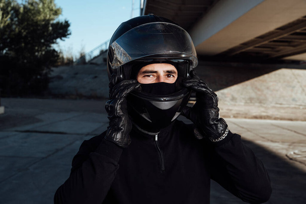 A handsome biker fastens his helmet. Motorcyclist puts on a helmet - Фото, изображение