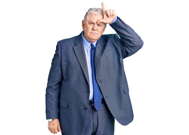Senior grey-haired man wearing business jacket making fun of people with fingers on forehead doing loser gesture mocking and insulting.  - Photo, Image