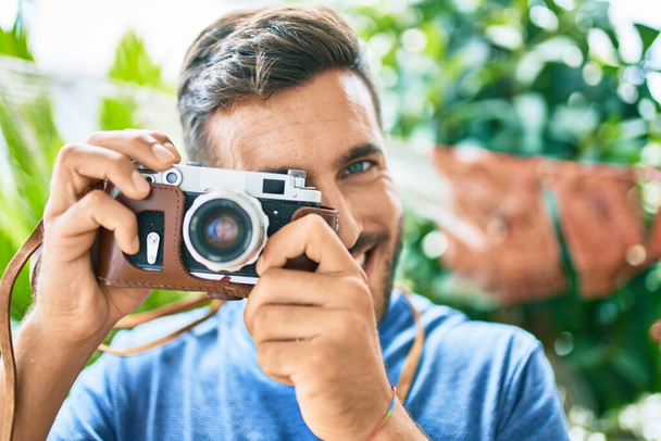 Jeune beau photographe souriant heureux en utilisant un appareil photo rétro au parc - Photo, image