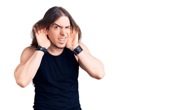 Young adult man with long hair wearing goth style with black clothes trying to hear both hands on ear gesture, curious for gossip. hearing problem, deaf  - Fotografie, Obrázek