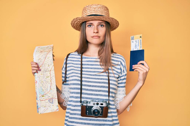 Beautiful caucasian tourist woman holding city map and passport relaxed with serious expression on face. simple and natural looking at the camera.  - Photo, Image