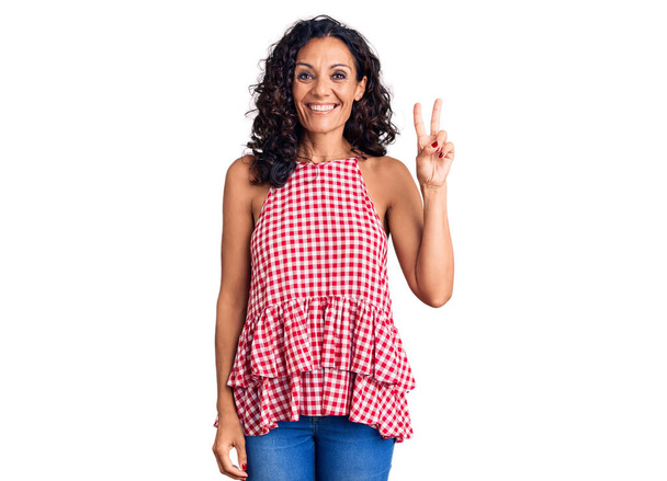 Middle age beautiful woman wearing casual sleeveless t shirt smiling with happy face winking at the camera doing victory sign. number two.  - Photo, Image