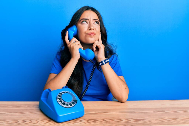 Красивая брюнетка молодая женщина говорит по старинному телефону серьезное лицо думая о вопросе с рукой на подбородке, вдумчивый о запутанной идее  - Фото, изображение