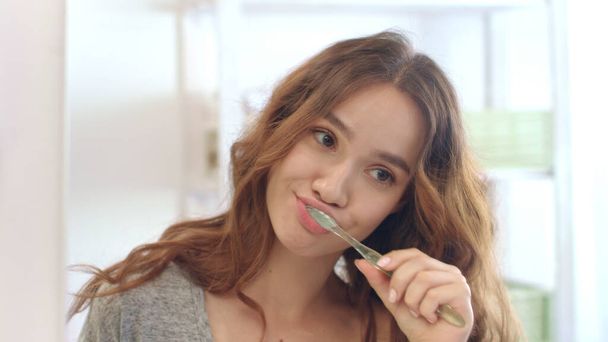 Mujer atractiva usando cepillo de dientes y pasta de dientes para cepillarse los dientes en el baño - Foto, imagen