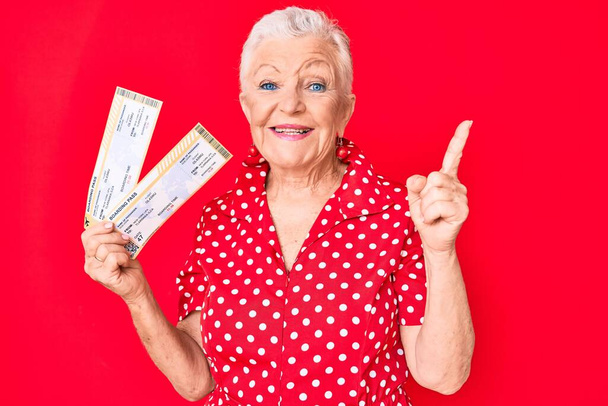 Senior beautiful woman with blue eyes and grey hair holding boarding pass smiling happy pointing with hand and finger to the side  - Foto, afbeelding