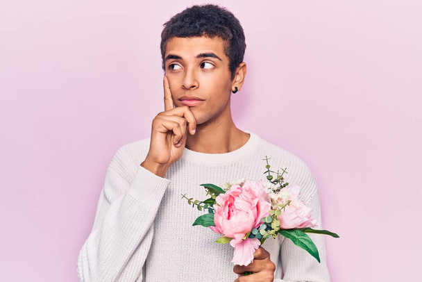 若いアフリカ系アメリカ人の男は深刻な顔の花を保持顎に手で質問について考えて、混乱のアイデアについて思慮深い  - 写真・画像