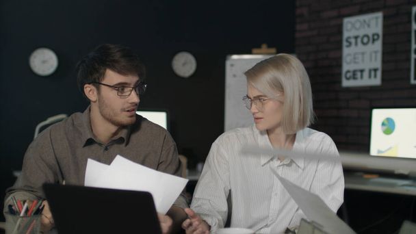 Young business man and woman working together front laptop in dark office - Photo, image