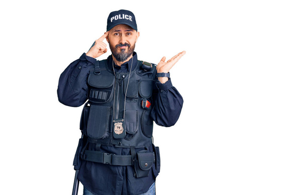 Joven hombre guapo vistiendo uniforme de policía confundido y molesto con la palma abierta mostrando espacio de copia y señalando con el dedo a la frente. Piénsalo.  - Foto, Imagen