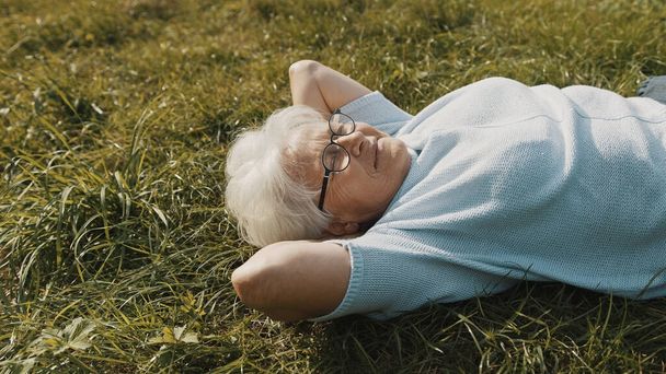 Coole Oma, die mit den Händen unterm Kopf im Gras liegt. Ruhe in der Natur - Foto, Bild