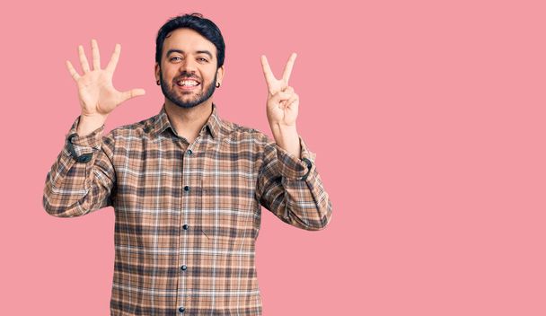Jeune homme hispanique portant des vêtements décontractés montrant et pointant vers le haut avec les doigts numéro sept tout en souriant confiant et heureux.  - Photo, image